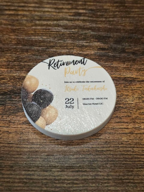 Circular retirement party invitation with beige and black stone design on wooden surface