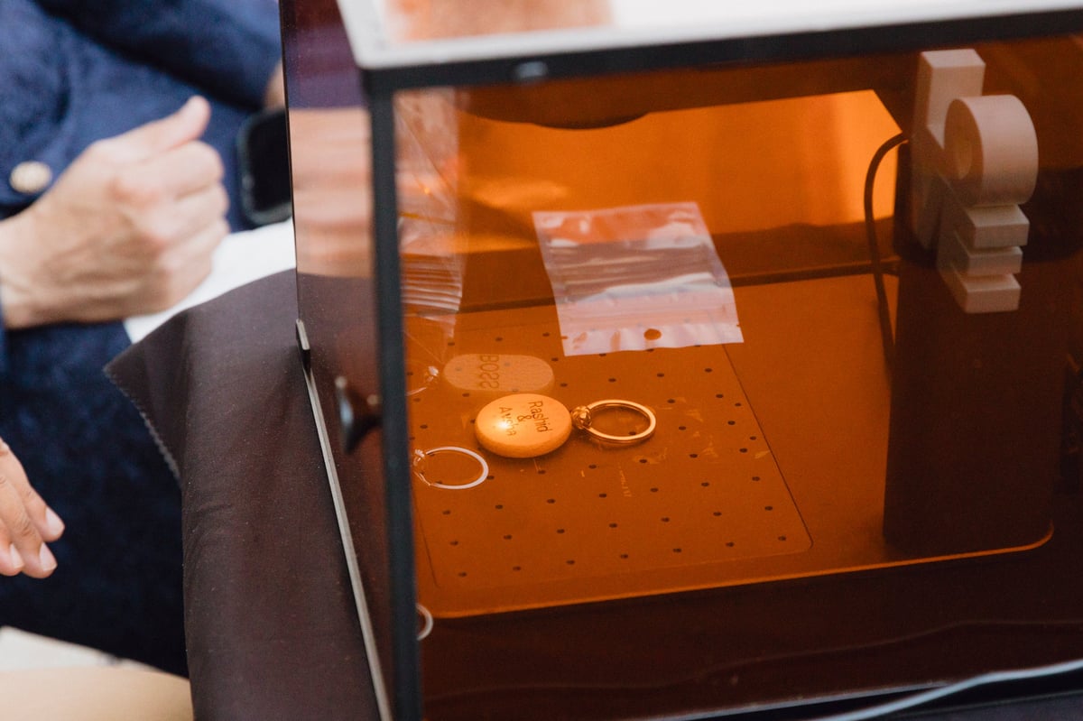 3D printer with orange build platform printing small circular objects and rings inside clear chamber