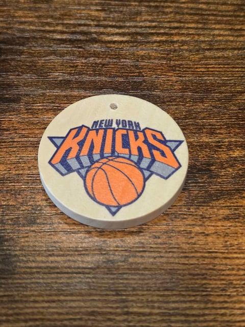 New York Knicks logo on a circular white pendant against a wooden surface