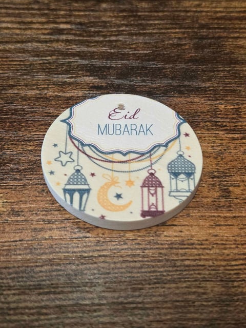 Round Eid Mubarak greeting card with lanterns, moon, and stars on wooden surface
